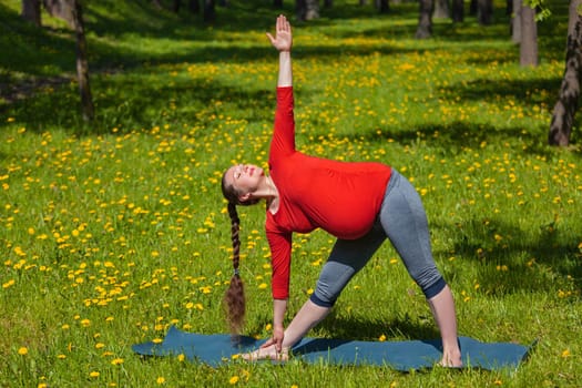 Pregnancy yoga exercise - pregnant woman doing asana Utthita trikonasana outdoors on grass in summer