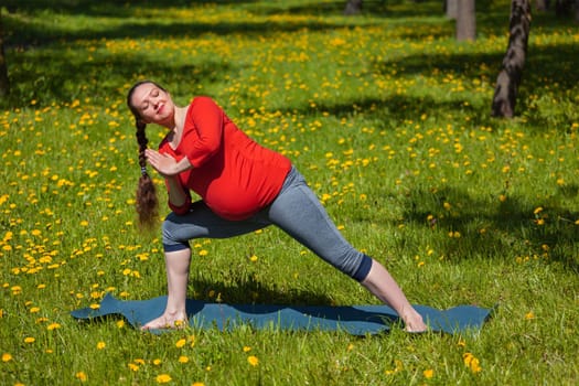 Pregnancy yoga exercise - pregnant woman doing asana Utthita parsvakonasana outdoors on grass in summer