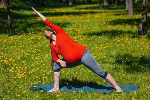 Pregnancy yoga exercise - pregnant woman doing asana Utthita parsvakonasana outdoors on grass in summer