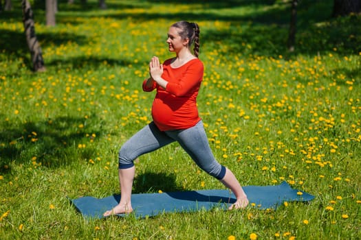 Pregnancy yoga exercise - pregnant woman doing yoga asana Virabhadrasana warrior pose outdoors on grass in summer