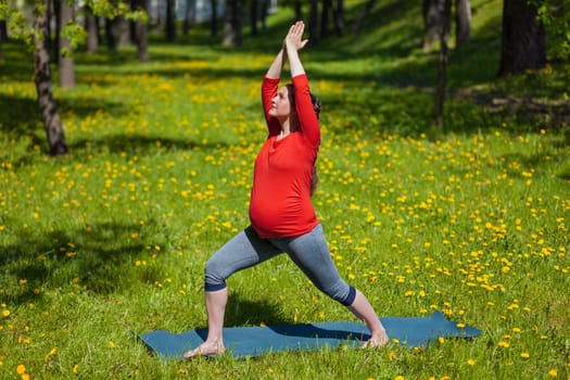 Pregnancy yoga exercise - pregnant woman doing yoga asana Virabhadrasana warrior pose outdoors on grass in summer