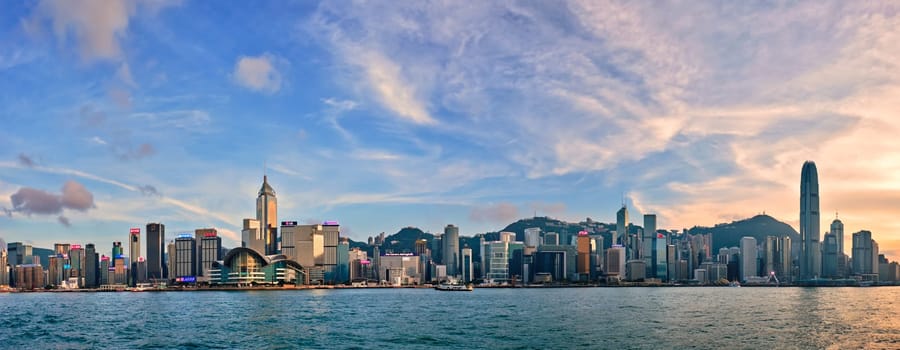 HONG KONG, CHINA - MAY 1, 2018: Panorama of Hong Kong skyline downtown skyscrapers over Victoria Harbour in evening with junk tourist ferry boat on sunset and dramatic sky. Hong Kong, China
