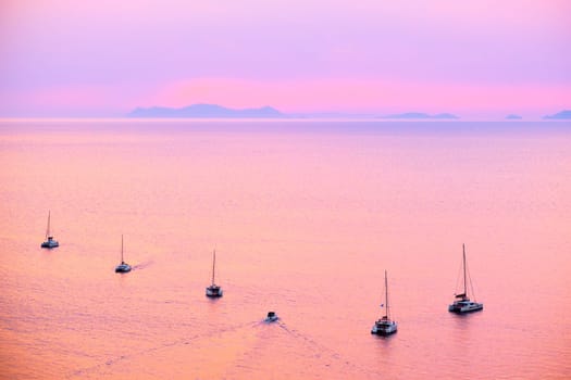 Tourist yachts boat in Aegean sea near Santorini island with tourists watching sunset from viewpoint. Santorini, Greece