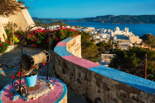 Picturesque scenic view of Greek town Plaka on Milos island over red geranium flowers and Orthodox greek church. Plaka village, Milos island, Greece