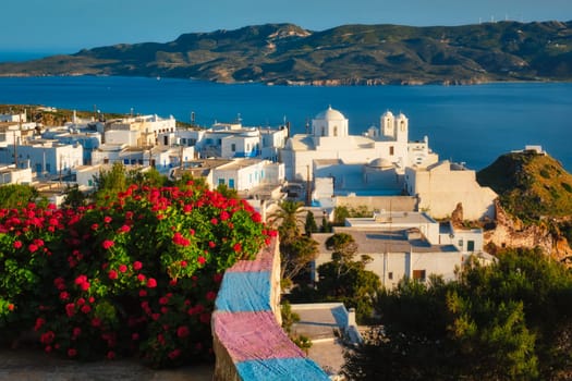 Picturesque scenic view of Greek town Plaka on Milos island over red geranium flowers and Orthodox greek church. Plaka village, Milos island, Greece. Focus on flowers