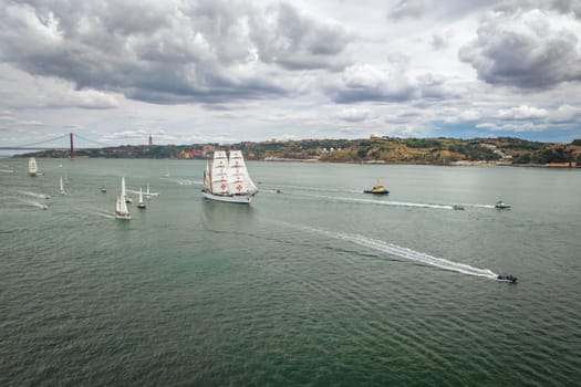 Aerial drone view of tall ships with sails sailing in Tagus river towards the Atlantic ocean in Lisbon, Portugal