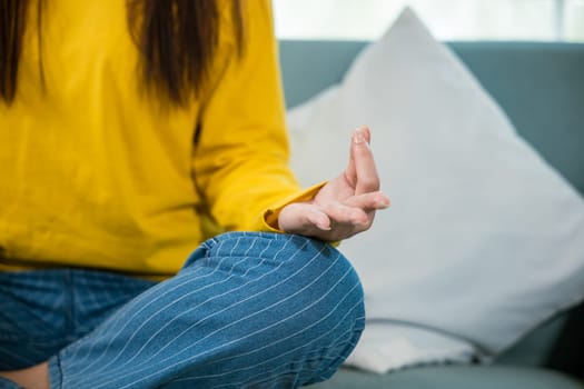 Young woman practise yoga and meditation in lotus position, mindfulness lifestyle, Asian female sits on sofa at home and chilling do yoga exercise with couch lotus pose eyes closed, healthy care