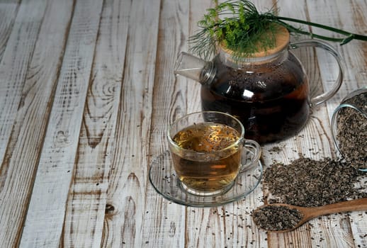Medicinal tea using dried dill seeds in a cup and teapot on a natural wooden table.
