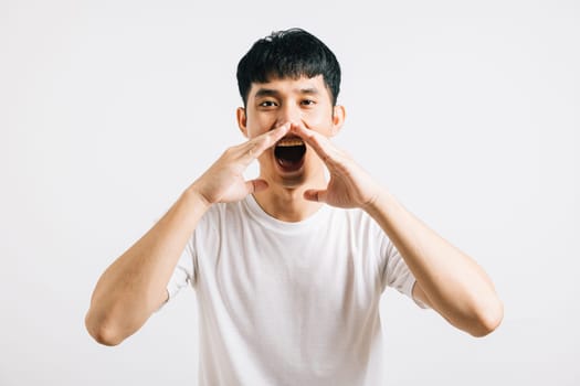 Portrait of a happy Asian young man with his hand on his mouth, sharing exciting news or announcements. Studio shot isolated on a white background, leaving room for copy space.