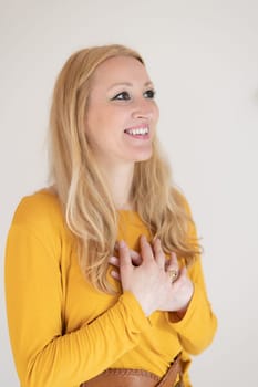 Portrait of cheerful confident beautiful woman with long blond hair, wearing casual clothes, standing in relaxed pose with hands on chest, breathing deeply, doing breathing exercise.