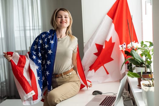 Happy woman employee sitting wrapped in USA flag, shouting for joy in office workplace, celebrating labor day or US Independence day. High quality photo