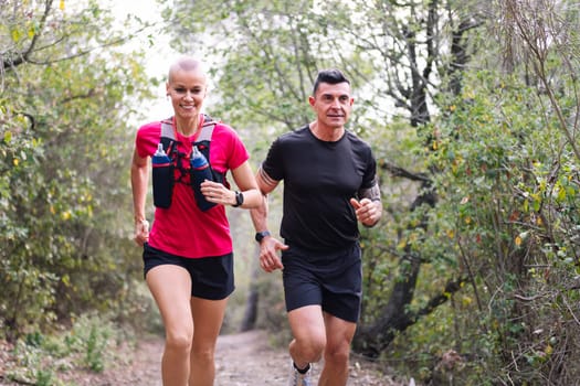 portrait of a happy couple practicing trail running in the woods, concept of sport in nature and healthy lifestyle, copy space for text