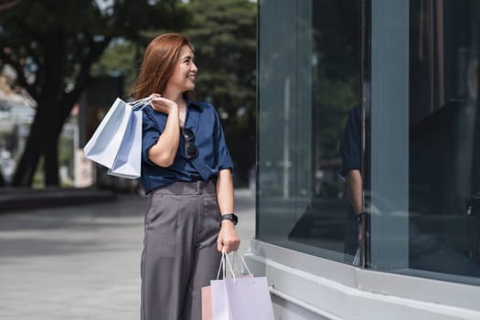 Happy tourist woman asian with shopping bags walks through the sunny street. Beautiful woman enjoys the weather after shopping. Consumerism, shopping. Active lifestyle.