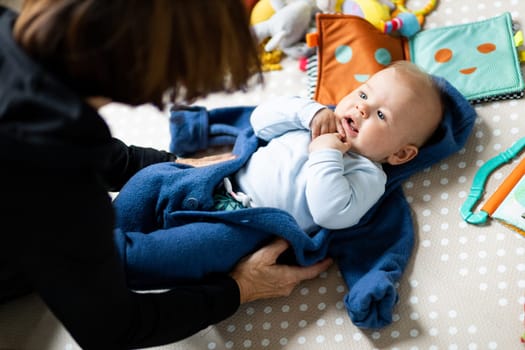 Happy family moments. Grandmother dressing up her grandson baby boy while he is laying on children's playing mat Positive human emotions, feelings, joy