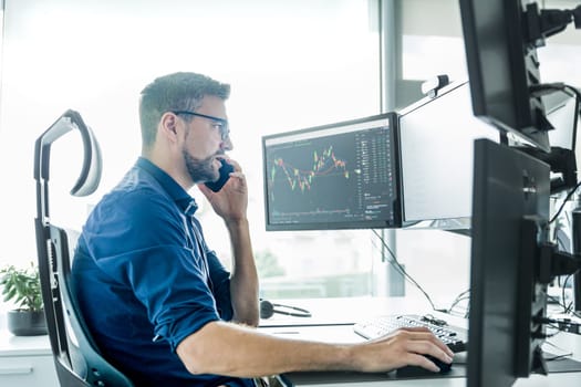 Male stock broker trading online watching charts and data analyses on multiple computer screens.