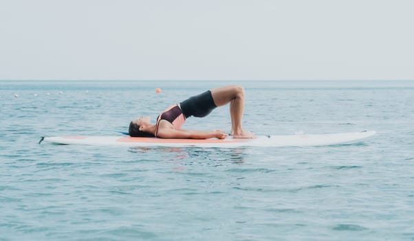 Woman sup yoga. Happy young sporty woman practising yoga pilates on paddle sup surfboard. Female stretching doing workout on sea water. Modern individual female outdoor summer sport activity