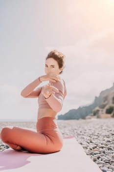 Young woman with long hair in white swimsuit and boho style braclets practicing outdoors on yoga mat by the sea on a sunset. Women's yoga fitness routine. Healthy lifestyle, harmony and meditation