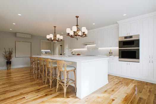 Traditional white kitchen with long island and wooden chairs with varnished wood flooring. Classic kitchen with large chandeliers and kitchen appliances. 3d rendering