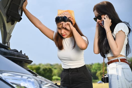 Female travelers looking under hood of her broke down car and calling for technician or insurance to help.