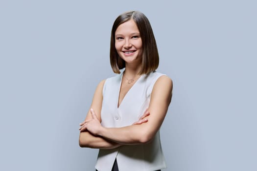 Portrait of young confident woman on grey studio background. Successful fashionable female with crossed arms looking at camera. Business, work, services, education, fashion beauty professions