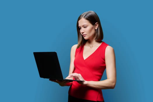Serious young business woman with laptop on blue studio background. Successful confident caucasian female looking at computer screen. Business, work, job, study, education, e-learning, technology