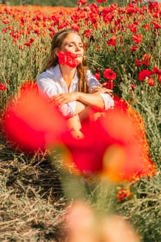 Woman poppies field. Happy woman is resting in the rays of the sun sitting in the poppy field