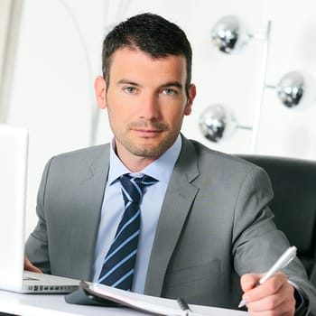 An attractive business man is writing on a paper
