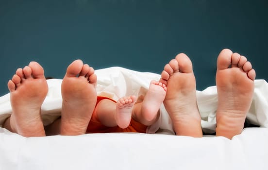 Tree pairs of legs of the happy family in bed - father, mother and baby