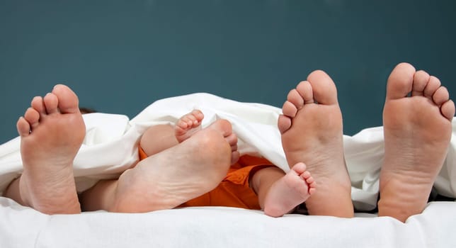 Tree pairs of legs of the happy family in bed - father, mother and baby