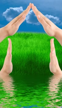 Conceptual home symbol from human hands on nature background