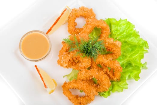 Deep-fried squid with salad leaves, sauce, green and lemon on a white background