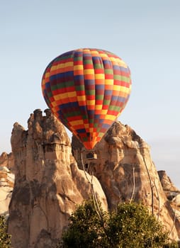 hot air harlequin balloon negotiates through limestone rocks, clear blue sky, early morning sun, portrait, copy space, crop area