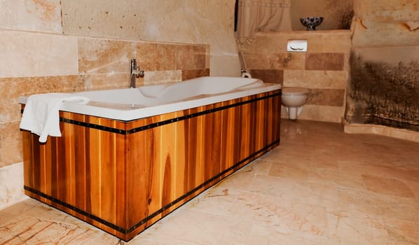 bathroom interior with wood panel bath tub, chrome center taps and toilet bowl, horizontal with crop space