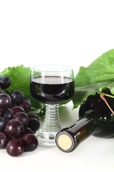 a bottle of red wine and fresh grapes against a white background