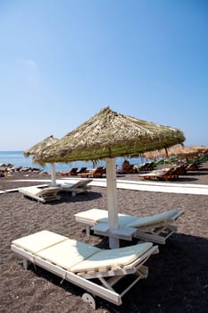 Beach umbrellas and sunbeds in morning sun in Perissa beach, Santorini, Greece