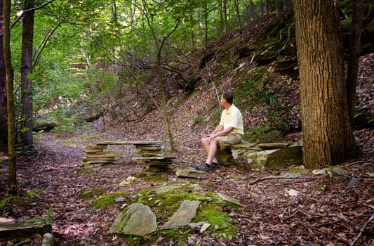 Retired hiker rests on stone benches in a clearing in a forest on a hike