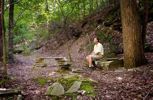 Retired hiker rests on stone benches in a clearing in a forest on a hike