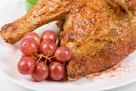 Half roasted chicken closeup with grape on a white