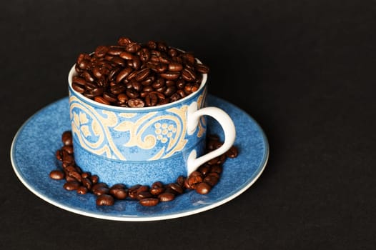 A cup and saucer overflowing with dark roasted coffee beans