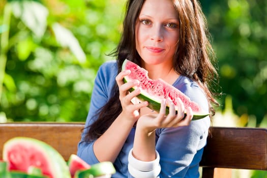 Beautiful young woman eating fresh melon sunny day garden bench