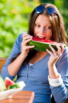 Beautiful young woman eating fresh melon sunny day garden bench