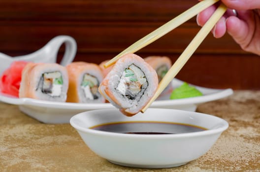 hand holding sushi with chopsticks at table