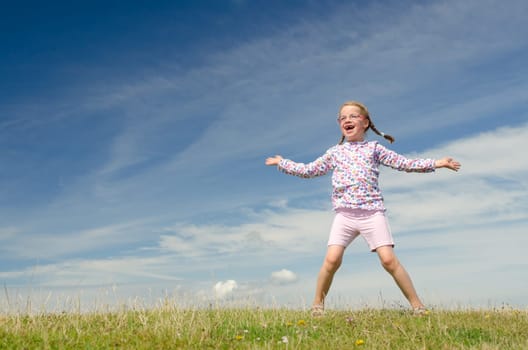 Young girl jumping on a green meadow against blue sky