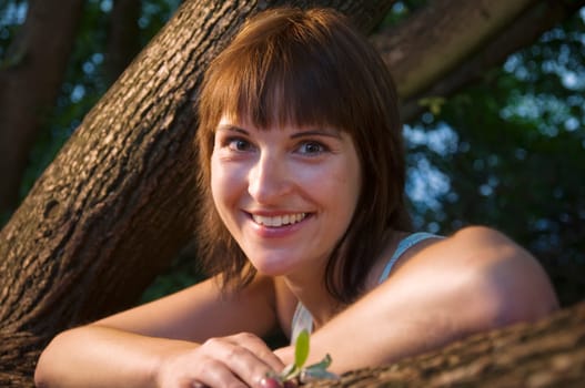 Head and shoulders portrait of a contentedly smiling young woman in a sleeveless top looking at the camera between a fork of a branch