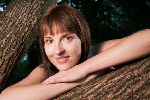Head and shoulders portrait of a contentedly smiling young woman in a sleeveless top looking at the camera between a fork of a branch