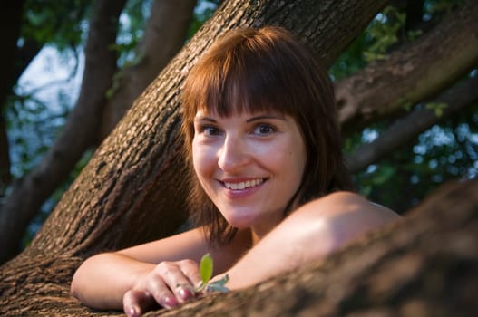 Head and shoulders portrait of a contentedly smiling young woman in a sleeveless top looking at the camera between a fork of a branch