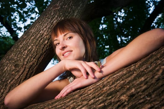 Head and shoulders portrait of a contentedly smiling young woman in a sleeveless top looking at the camera between a fork of a branch