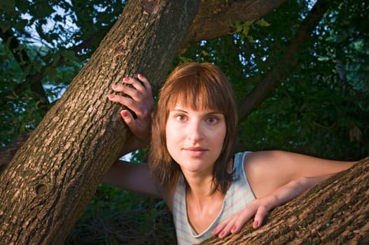 Head and shoulders portrait of a contentedly smiling young woman in a sleeveless top looking at the camera between a fork of a branch