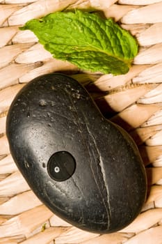 Black spa stone with a green leaf on wood mesh