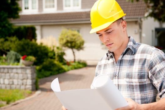 Young architect with a blueprint in front of a house